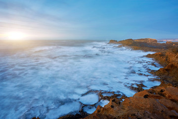 The stony coast of the Atlantic Ocean is washed by the waves during sunset, Essaouira