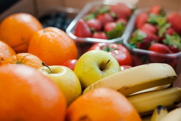 Delivery of fresh organic vegetables in box, local market food. Focus on fresh and colorful vegetables and fruits in a cardboard. Oranges, bananas, apples, tomatoes, strawberries and blueberries.
