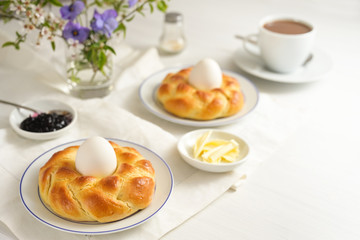 Easter yeast bread plaited in nest form with eggs, coffee, butter, jam and flowers on a white table, as a festive Sunday breakfast, copy space