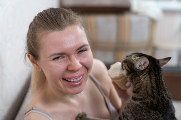 the girl sitting on the couch eats ice cream and the kitty also wants to feast on