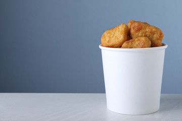 Bucket with tasty chicken nuggets on light grey table against blue background. Space for text