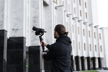 Young Professional videographer holding professional camera on 3-axis gimbal stabilizer. Pro equipment helps to make high quality video without shaking. Cameraman wearing black hoodie making a videos. © Volodymyr_sh