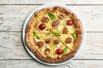 Delicious cheese pizza with walnuts and grapes on white wooden table, top view