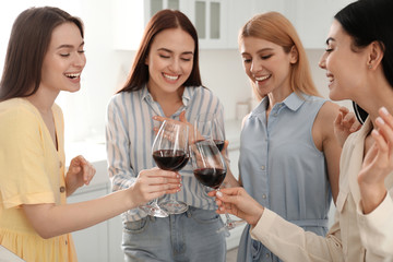 Fototapeta premium Beautiful young ladies clinking glasses of wine in kitchen. Women's Day