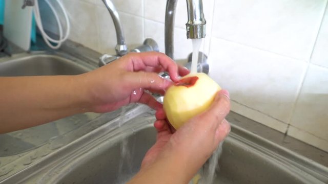 Lady hand wash fresh red apple on water sink