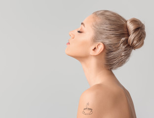Portrait of beautiful young woman with tattoo on grey background