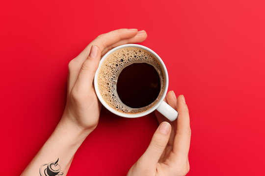 Female hands with cup of hot coffee on red background