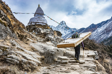 Sherpa die zwaar hout voor deuren draagt op weg naar het Everest-basiskamp, Himalaya-gebergte, Nepal.