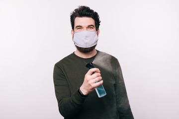 Photo of man with facial mask spraying with sanitizer over white background