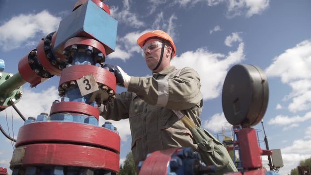 Oilman in orange helmet and protective glass closing valve of x-mass wellhead to shut off well. Decline in oil production after adoption of agreements at meeting of OPEC to stabilize price of oil.