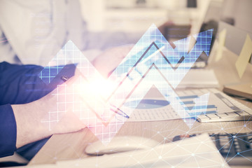 Double exposure of man's hands holding and using a digital device and arrows hologram drawing....