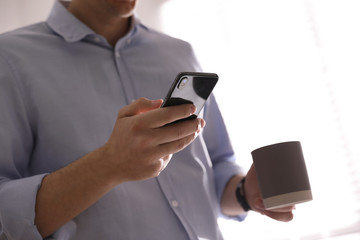 Man with cup and smartphone against light background, closeup of hands