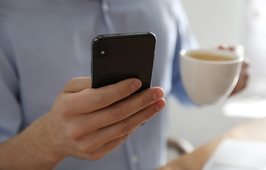 Man with smartphone indoors, closeup of hand