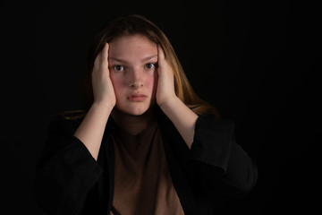 Sad teen girl on a black background with head in hands.