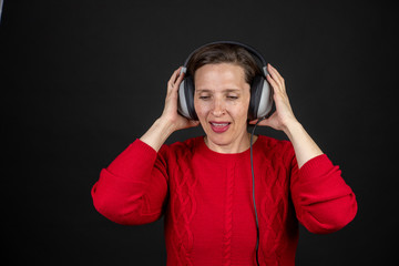 Older woman with a set of retro corded headphones in a red sweater dancing and enjoying music.