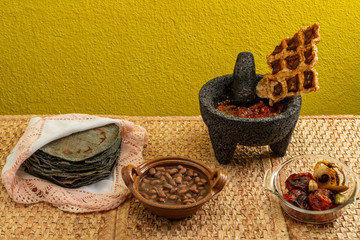 Fototapeta na wymiar Beans from the pot, a typical Mexican dish, accompanied by pork rinds, a molcajete with tomato sauce, chili, garlic, onion and salt, as well as handmade tortillas.