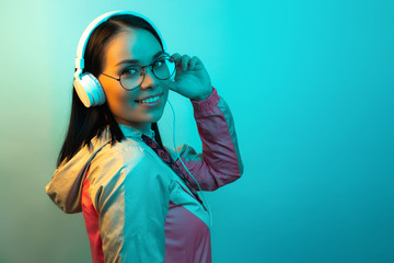 Pretty young woman with white headphones listening to music in neon lights at studio.