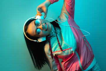 Happy young woman in 90s style sport outfit with white headphones dance in neon lights at studio.