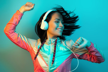 Careless young woman in 90s style sport outfit with white headphones dance in neon lights at studio.