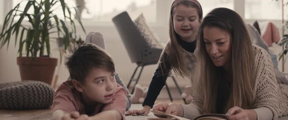 Mother daughter and son enjoying reading a book 
 education family time during coronavirus covid 19 pandemic outbreak wellbeing staying home in isolation - Powered by Adobe