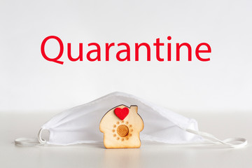 Small wooden house shape covered with medical protective face mask and word Quarantine on white background. Covid-19 lockdown, isolation, stop pandemic coronavirus concept.