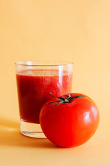  RED TOMATO NEXT TO GLASS WITH TOMATO JUICE AND YELLOW BACKGROUND