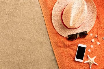 Summer fashion, summer outfit on sand background. Smartphone, sunglasses and straw hat. Flat lay,...