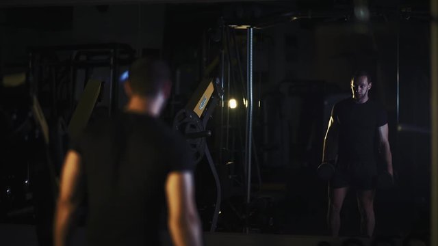 Reflection in a mirror strong athletic men pumping up muscles - muscular bodybuilder handsome men doing exercises lifting dumbbells to biceps in gym slow motion. 50 fps