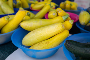 Yellow squash in blue bowls and green zucchini on a table at a farmer's market. The squash has a flat bottom and tappers along its long body at the neck. The small vegetables are laid in small bowls.