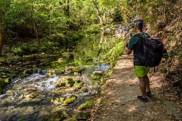 Hombre excursionista joven de espaldas tomando foto en selva con r&iacute;o