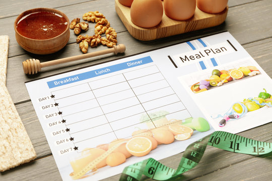 Healthy products and meal plan with measuring tape on wooden background