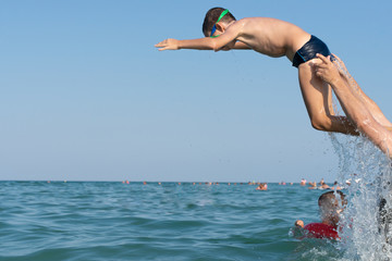 Fototapeta na wymiar Father, playing with children at the seaside. Executing water jumps. Boy flying in midair.