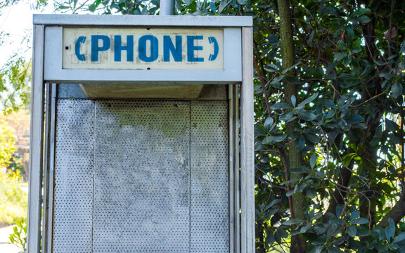 close up of an abandoned vintage telephone booth with blank wall for customized message, amid overgrown trees and weeds