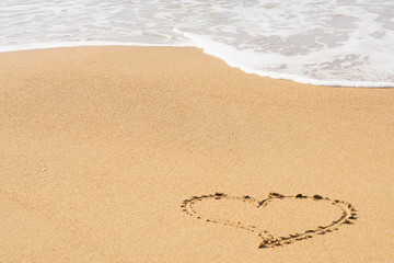 A heart symbol written on a sandy beach with foam and water background. Valentines day concept.