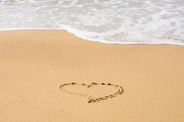 A heart symbol written on a sandy beach with foam and water background. Valentines day concept.