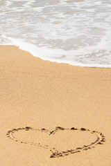 Fototapeta na wymiar A heart symbol written on a sandy beach with foam and water background. Valentines day concept.