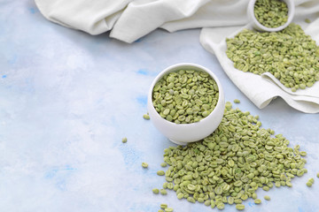 Bowl with green coffee beans on color background