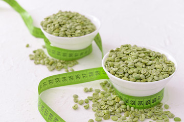 Bowls with green coffee beans and measuring tape on white background