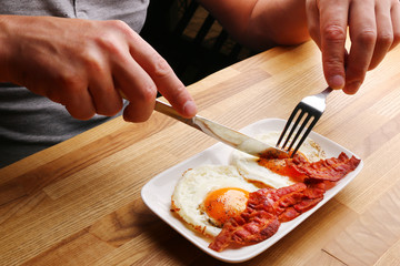 man having breakfast. male hands cutting fried egg with bacon. breakfast concept