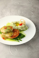 fish cutlet on asparagus with potato and sauce on white plate