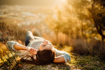Carefree happy woman lying on green grass meadow on top of mountain enjoying sun on her face.Enjoying nature sunset.Freedom.Relaxing in mountains at sunrise.Sunshine.Daydreaming.Listening to music