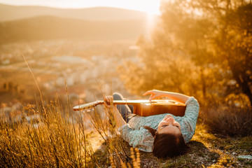 Young guitarist playing acoustic guitar and looking to sunset.Searching inspiration.Music creator.New artist in good mood.Musical talent.Smiling young woman singing and playing acoustic guitar. - obrazy, fototapety, plakaty