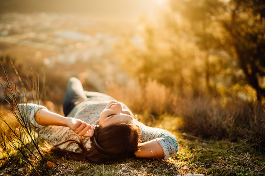 Carefree happy woman lying on green grass meadow on top of mountain enjoying sun on her face.Enjoying nature sunset.Freedom.Relaxing in mountains at sunrise.Sunshine.Daydreaming.Listening to music