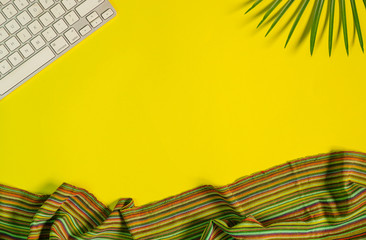 Top view of yellow color office table with keyboard, palm leaves and fabric.