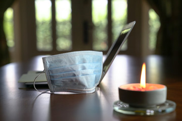 Work at home during coronavirus outbreak. Focus on face mask with computer laptop and burning candle on table