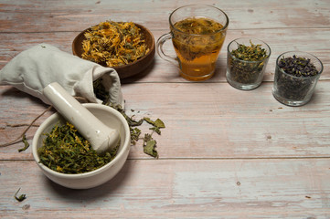 Phytotherapy. Composition of dry herbs for herbal medicine.  Herbal decoction of calendula and various dried herbs in linen bags and cups on a light wooden background. Free space.