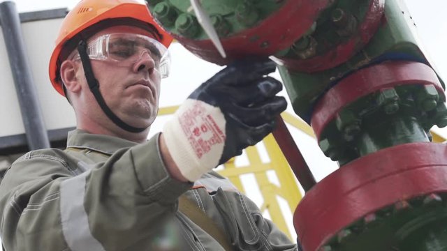 Oil field technical worker opening valve of wellhead to open well. Concept increase in oil production after collapse of OPEC talks.