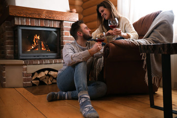 Obraz premium Lovely couple with glasses of wine near fireplace indoors. Winter vacation