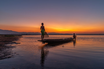 Picture of Asian fishermen on a wooden boat Thai fishermen catch fresh water fish in the natural river, traditional Thai fishermen at the morning sun on the lake of Thailand