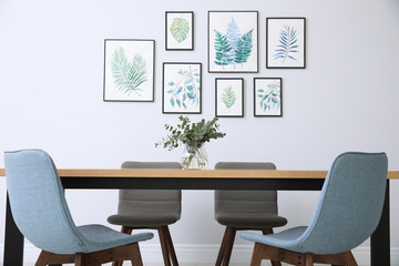Stylish room interior with modern table, chairs and paintings of tropical leaves. Idea for design